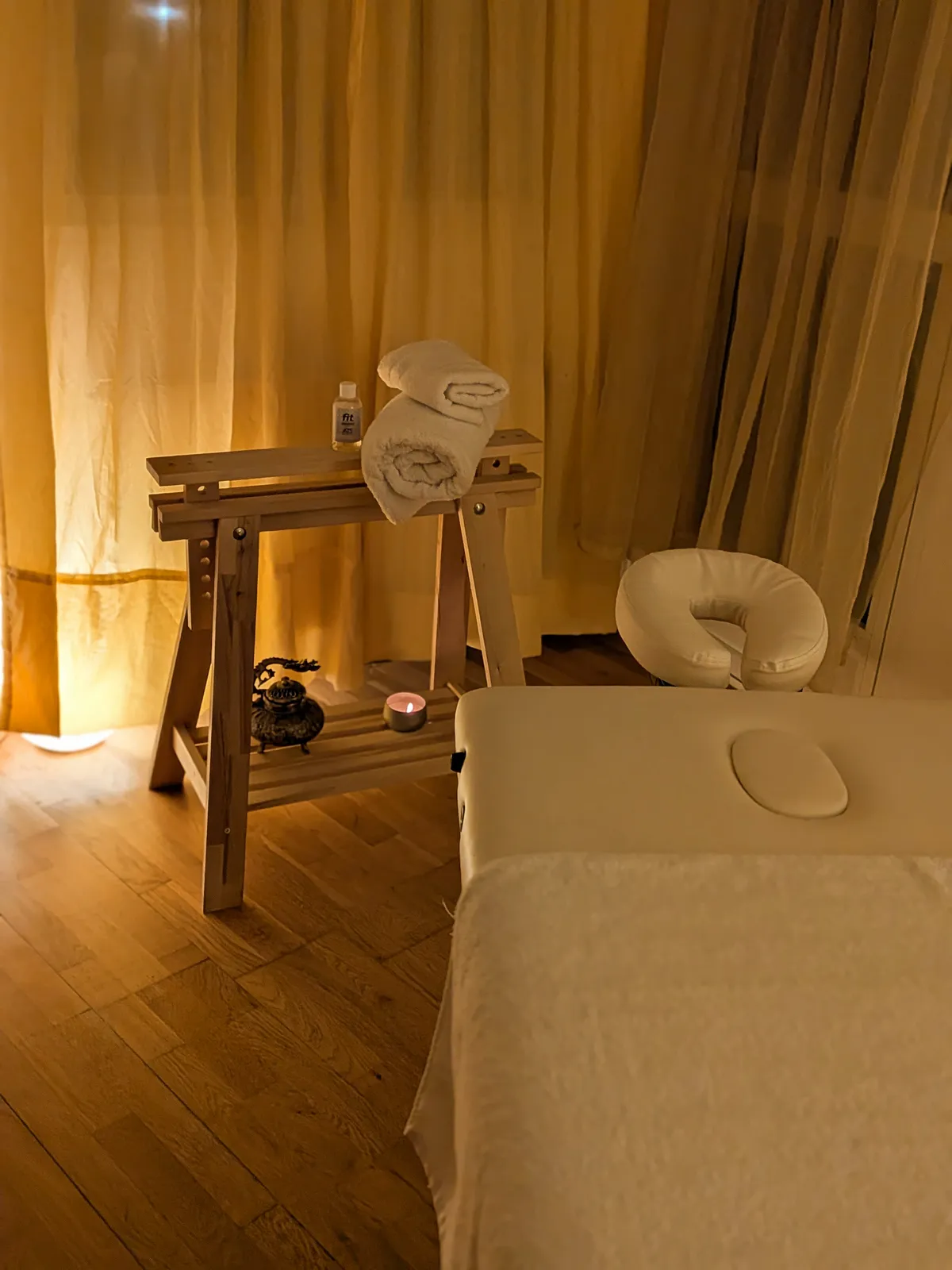 A warmly lit massage room with a treatment table, fresh towels, and a candle